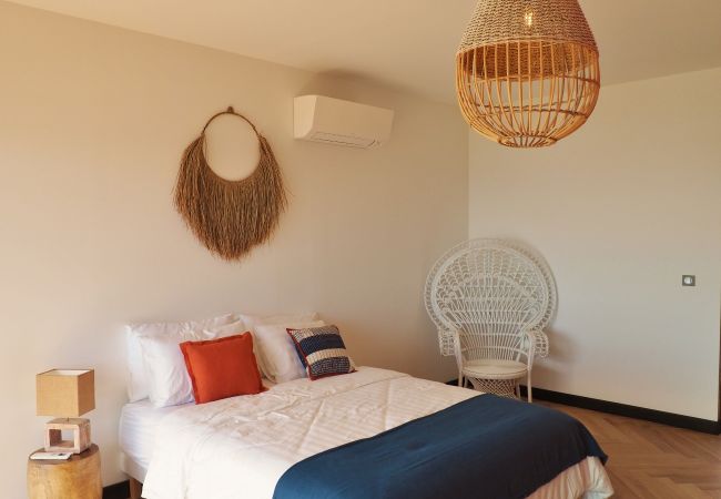 Chambre blanche avec lit double, fauteuil en rotin et climatisation – Villa Naézora, villa 10 personnes avec piscine à Saint-Gilles-les-Bains, La Réunion