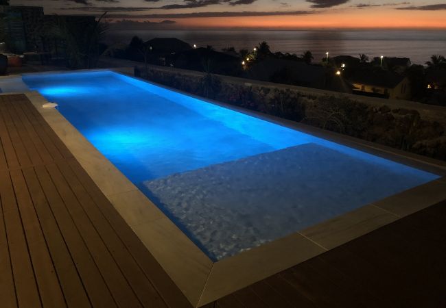 La piscine éclairée en bleu la nuit, face aux lumières de la côte – Villa Naézora, villa 10 personnes avec piscine à Saint-Gilles-les-Bains, La Réunion